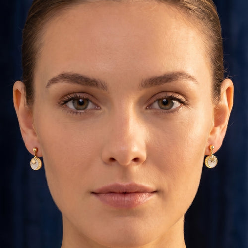 Woman wearing Engelsrufer sun moon & star gold earrings.