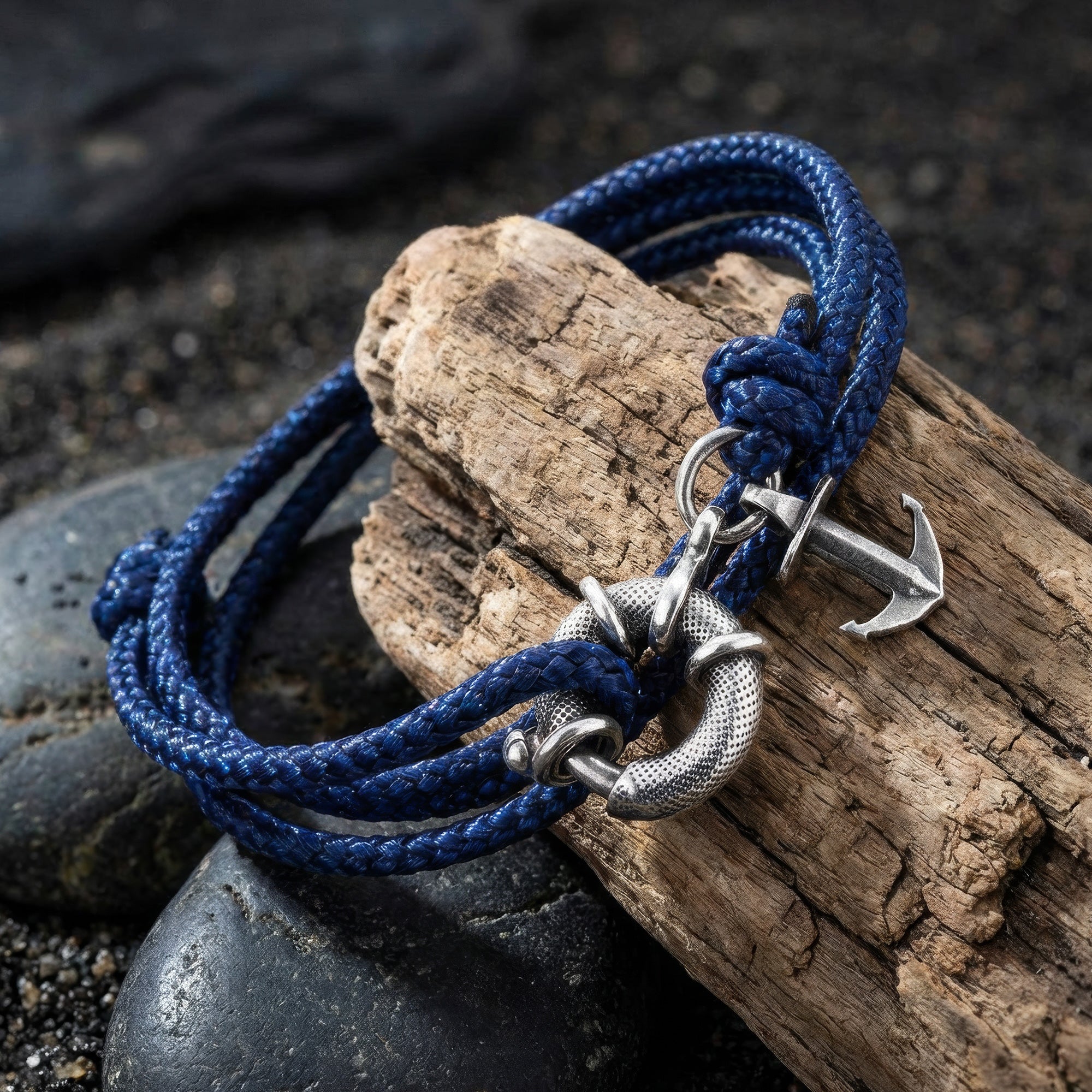Anchor & Crew Clyde sterling silver navy blue rope bracelet resting on a piece of wood and black pebbles.