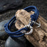 Anchor & Crew Clyde sterling silver navy blue rope bracelet resting on a piece of wood and black pebbles.