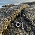 An Anchor & Crew Clyde anchor & life buoy sterling silver necklace laying on a barnacled seashore rock.