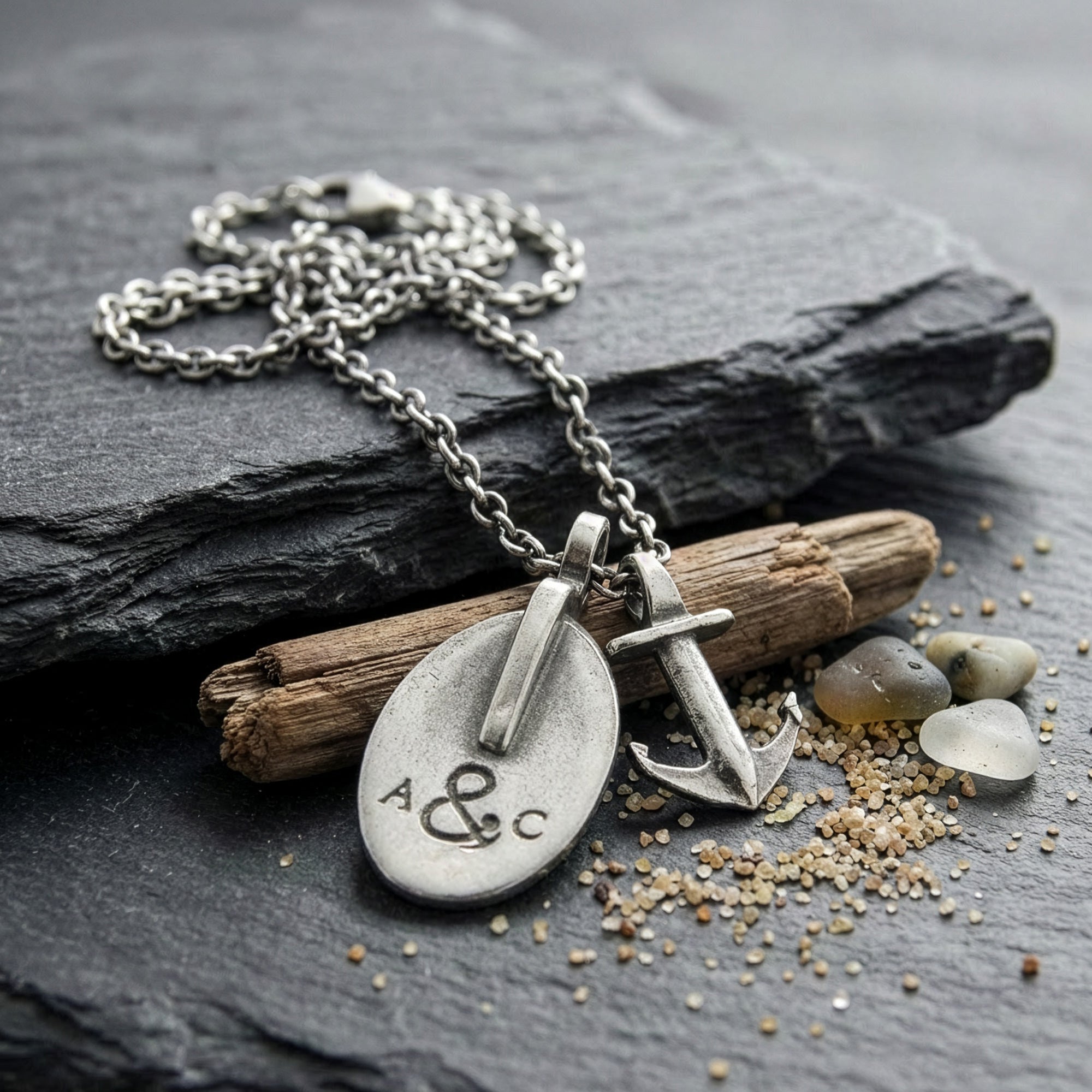 Anchor & Crew London pulley & anchor silver necklace on black slate amid beach flotsam.