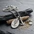 Anchor & Crew London pulley & anchor silver necklace on black slate amid beach flotsam.