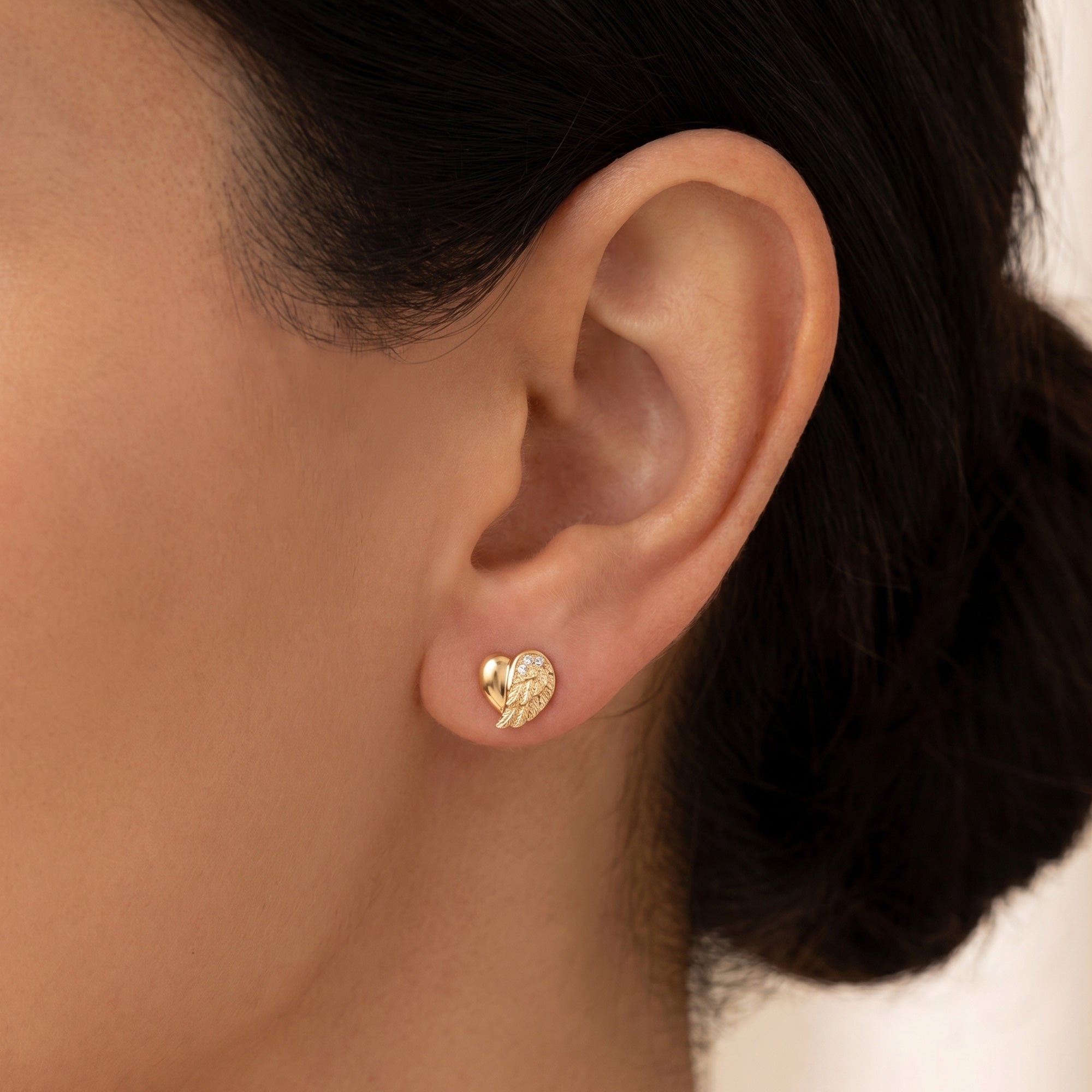 Woman wearing Engelsrufer angel wing heart gold CZ stud earrings.