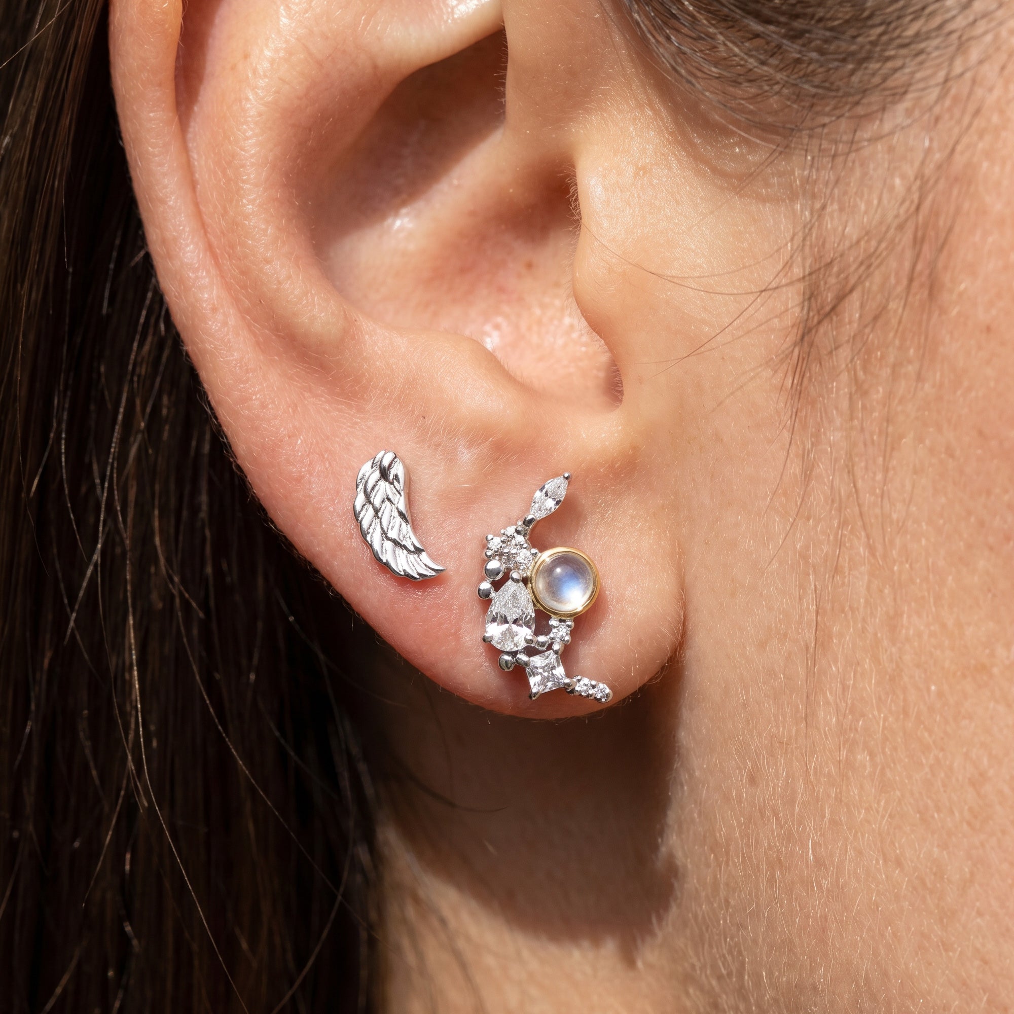 Close-up of woman wearing Engelsrufer angel wing & moon mismatch stud earrings.