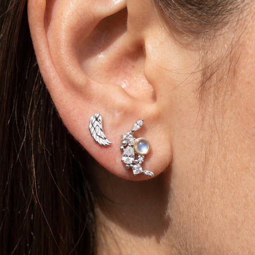 Close-up of woman wearing Engelsrufer angel wing & moon mismatch stud earrings.