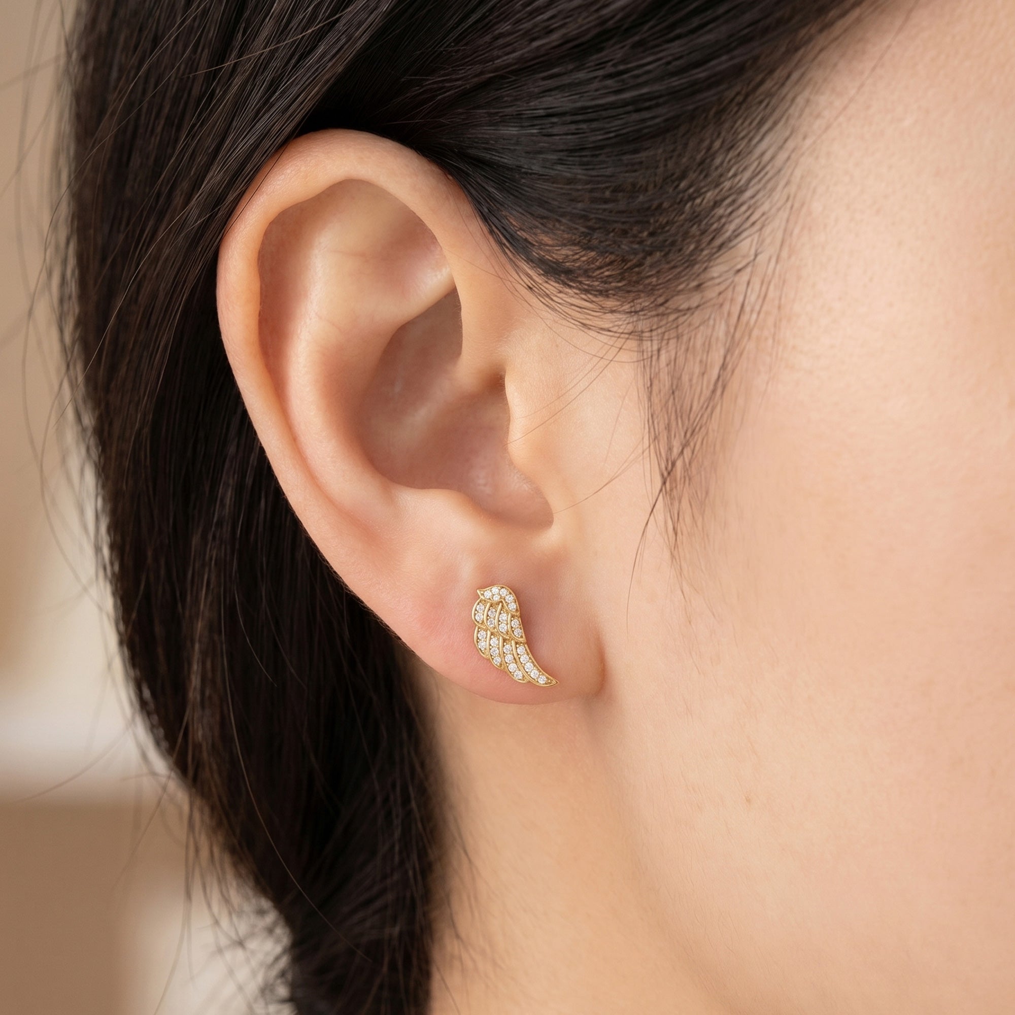Woman wearing Engelsrufer angel wing crystal pave gold stud earrings.