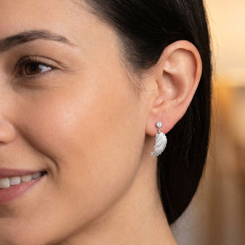 Woman wearing Engelsrufer angel wing feather CZ silver dangle earrings.