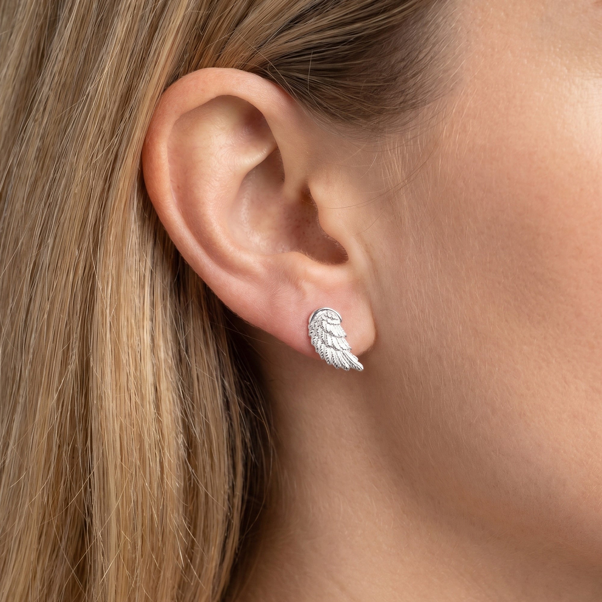 Woman wearing Engelsrufer angel wing silver stud earrings.