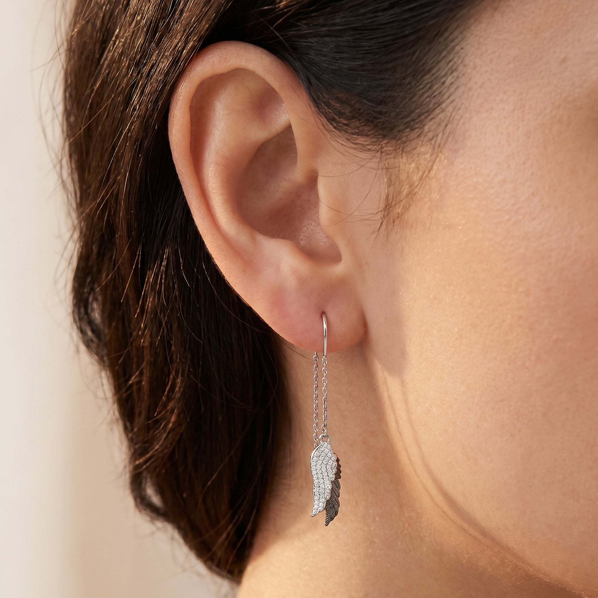 Woman wearing Engelsrufer angel wings duo thread CZ earrings.