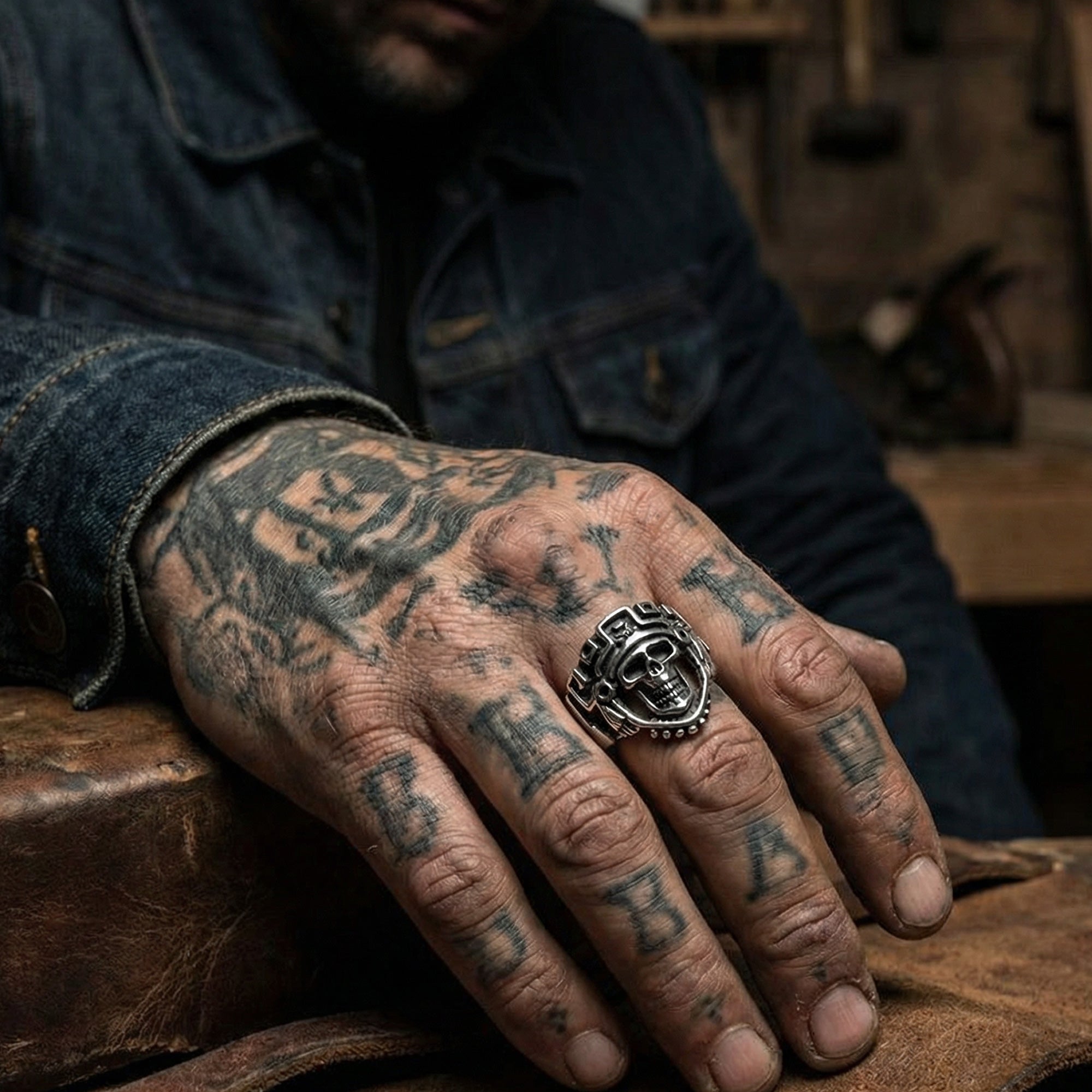 Man in denim jacket with hand tattoos wearing stainless steel men's skull Aztec death mask ring.