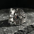 A winged barbed cross stainless steel men's ring sitting on a slab of dark grey stone,