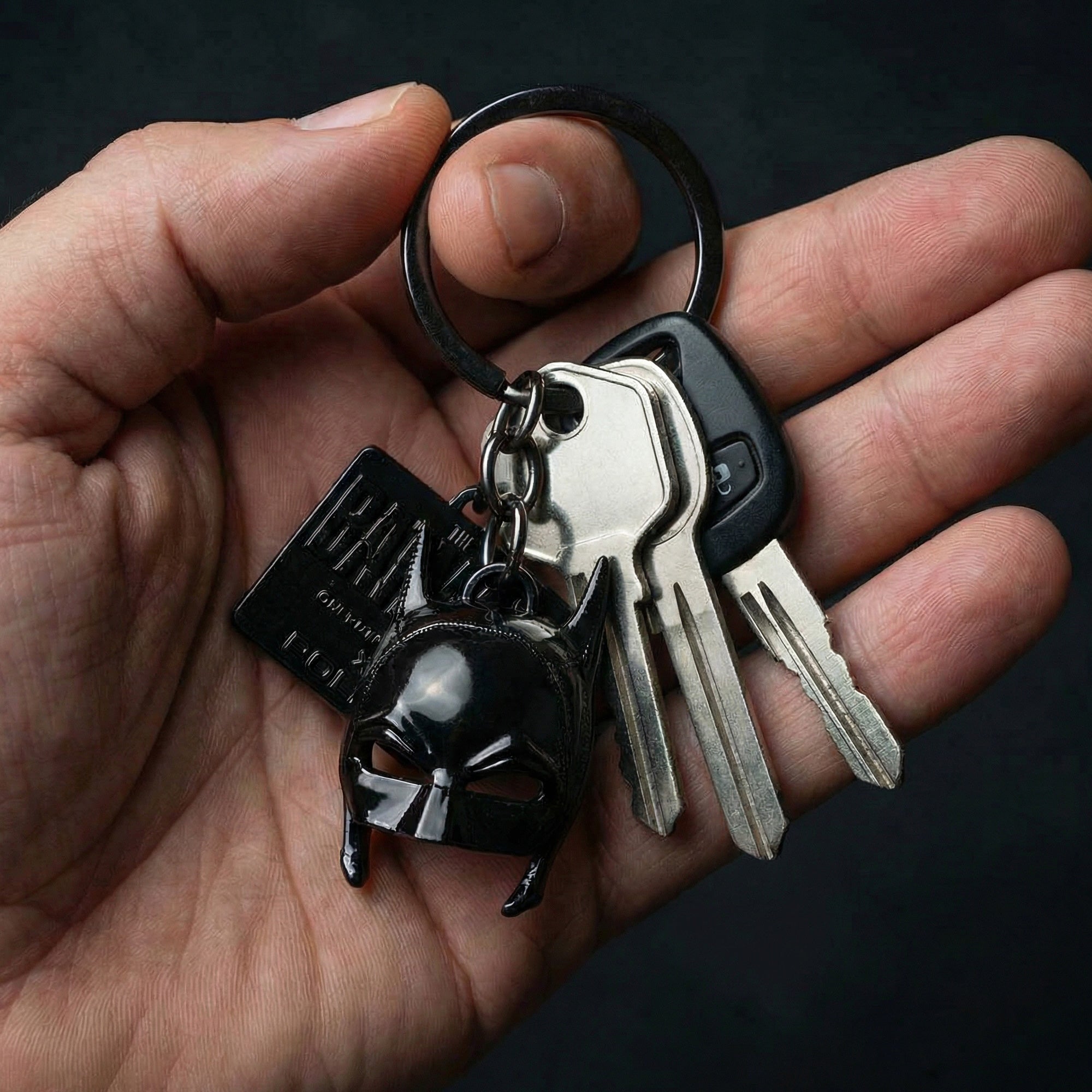 Batman cowl mask black steel keyring with keys attached being held in a man's hand.