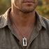 Close-up of a man in an open-collar shirt wearing a black cable steel dog tag necklace.