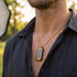 Close-up of a man in an open-neck shirt wearing a black and gold steel cable dog tag necklace.