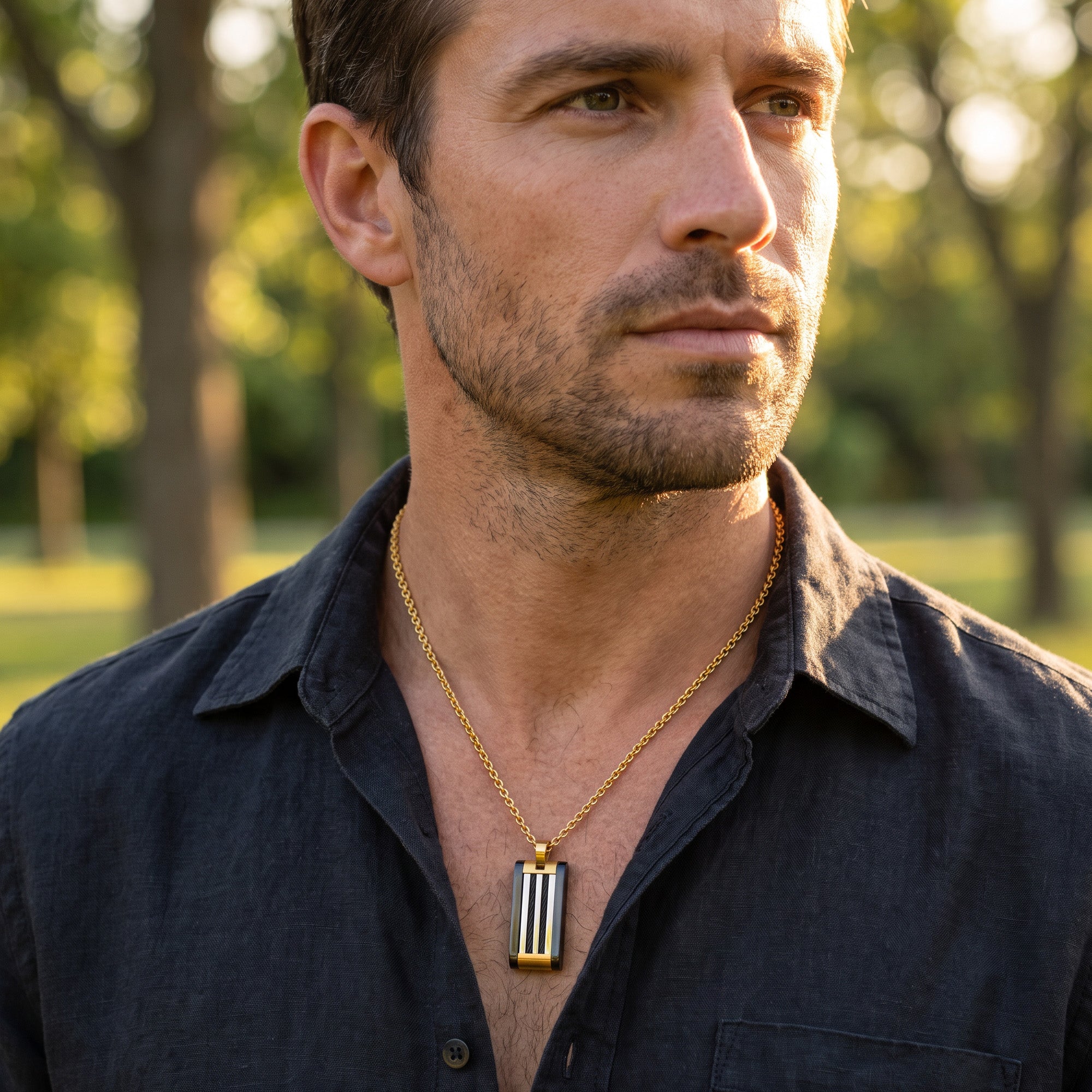 Man in an open-neck shirt wearing a black and gold steel cable dog tag necklace.