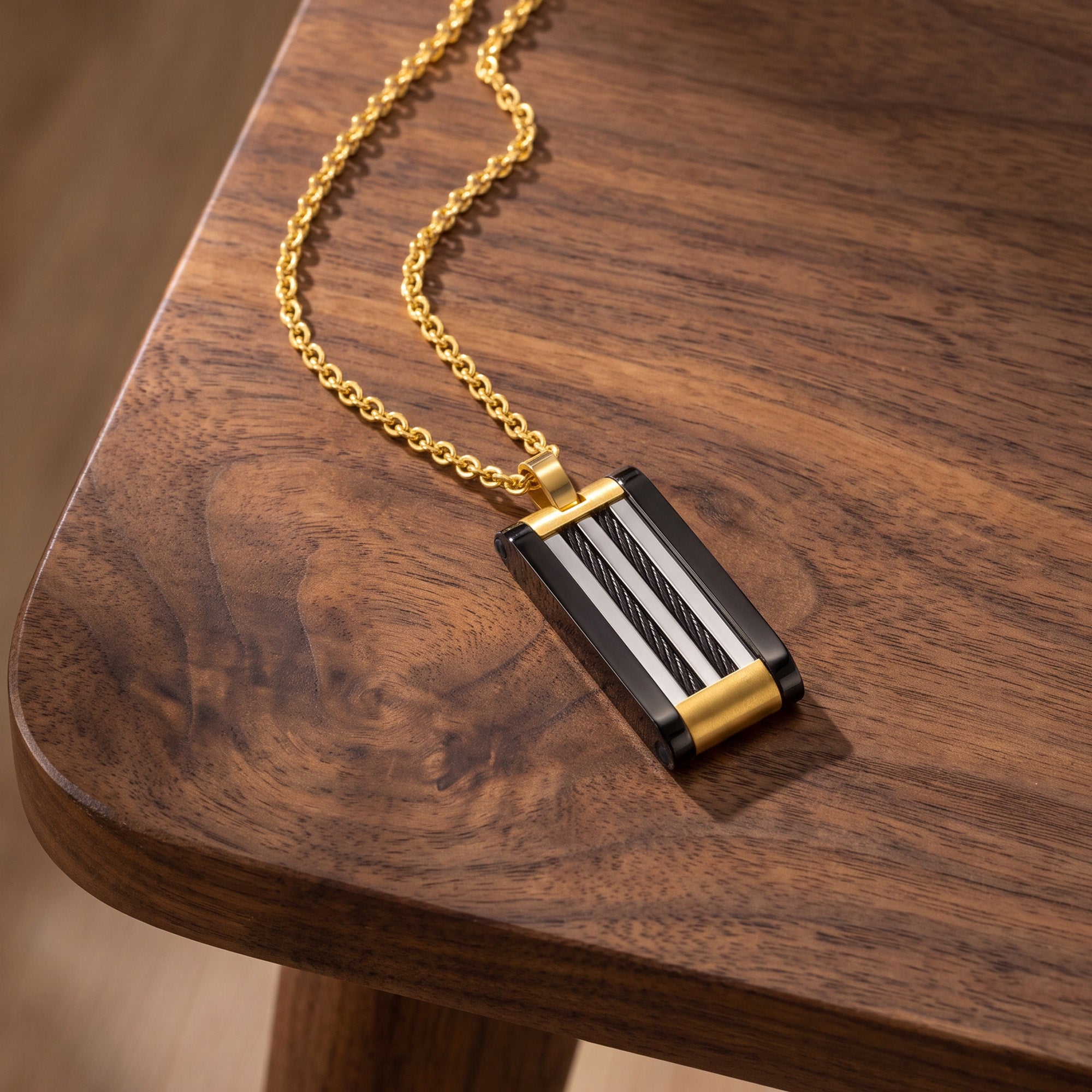 A black and gold steel cable dog tag men's necklace laying on the edge of a wooden table.