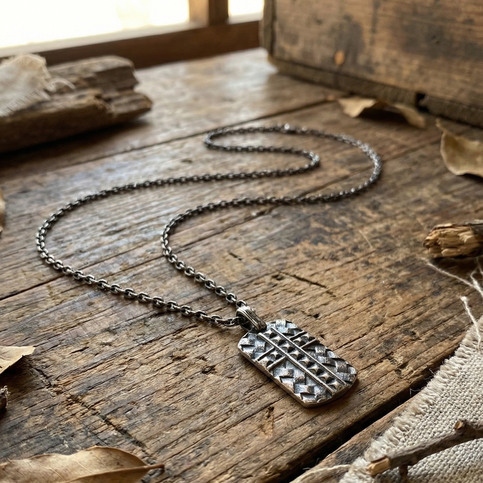 Black steel men's cross dog tag necklace laying on a wooden workshop bench.