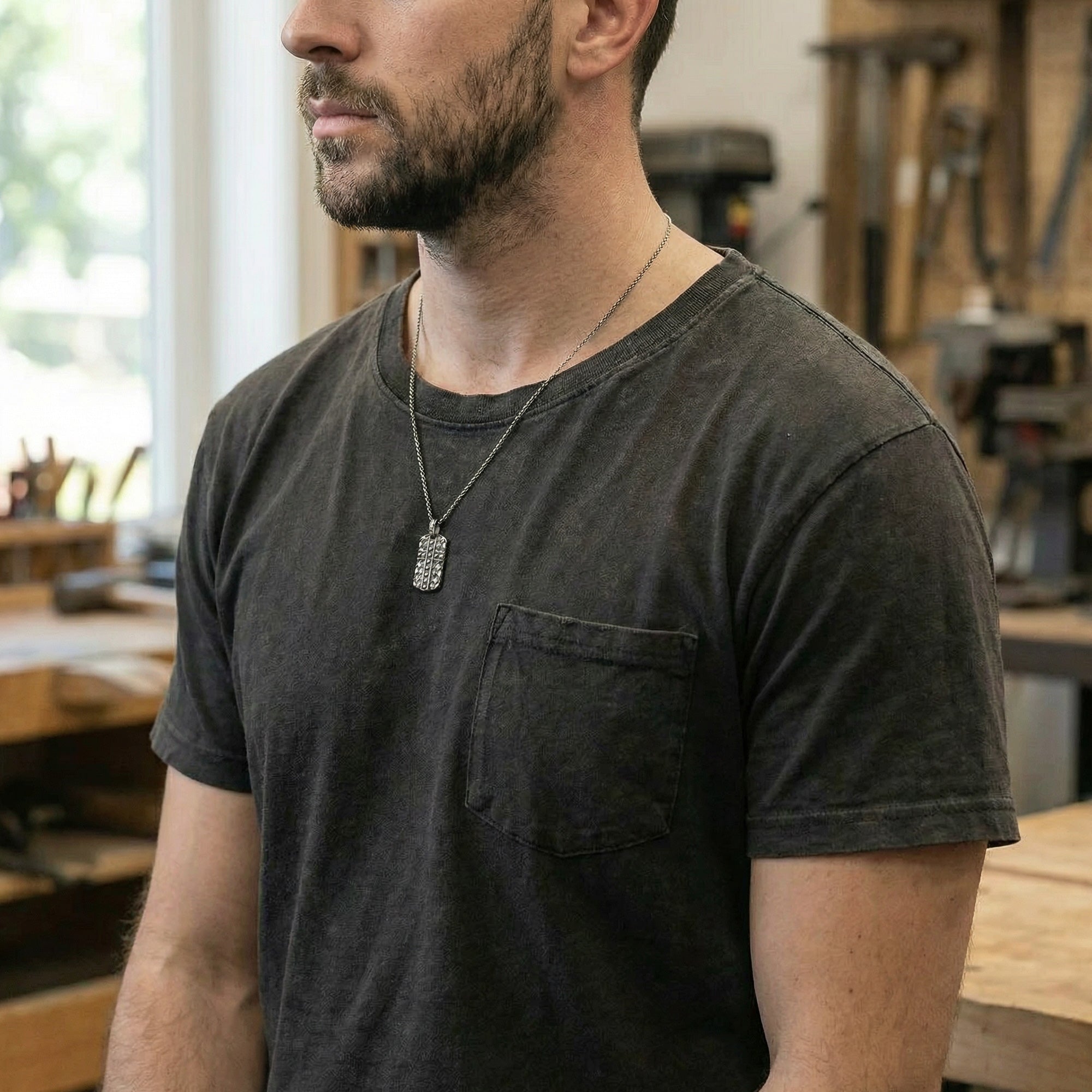 Man standing in a woodworking workshop wearing black steel men's cross dog tag necklace.