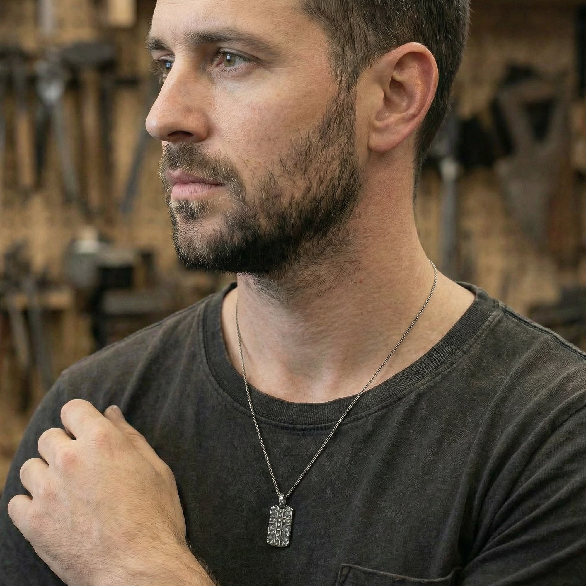 Man wearing black steel men's cross dog tag necklace looking to the left in a pensive mood.
