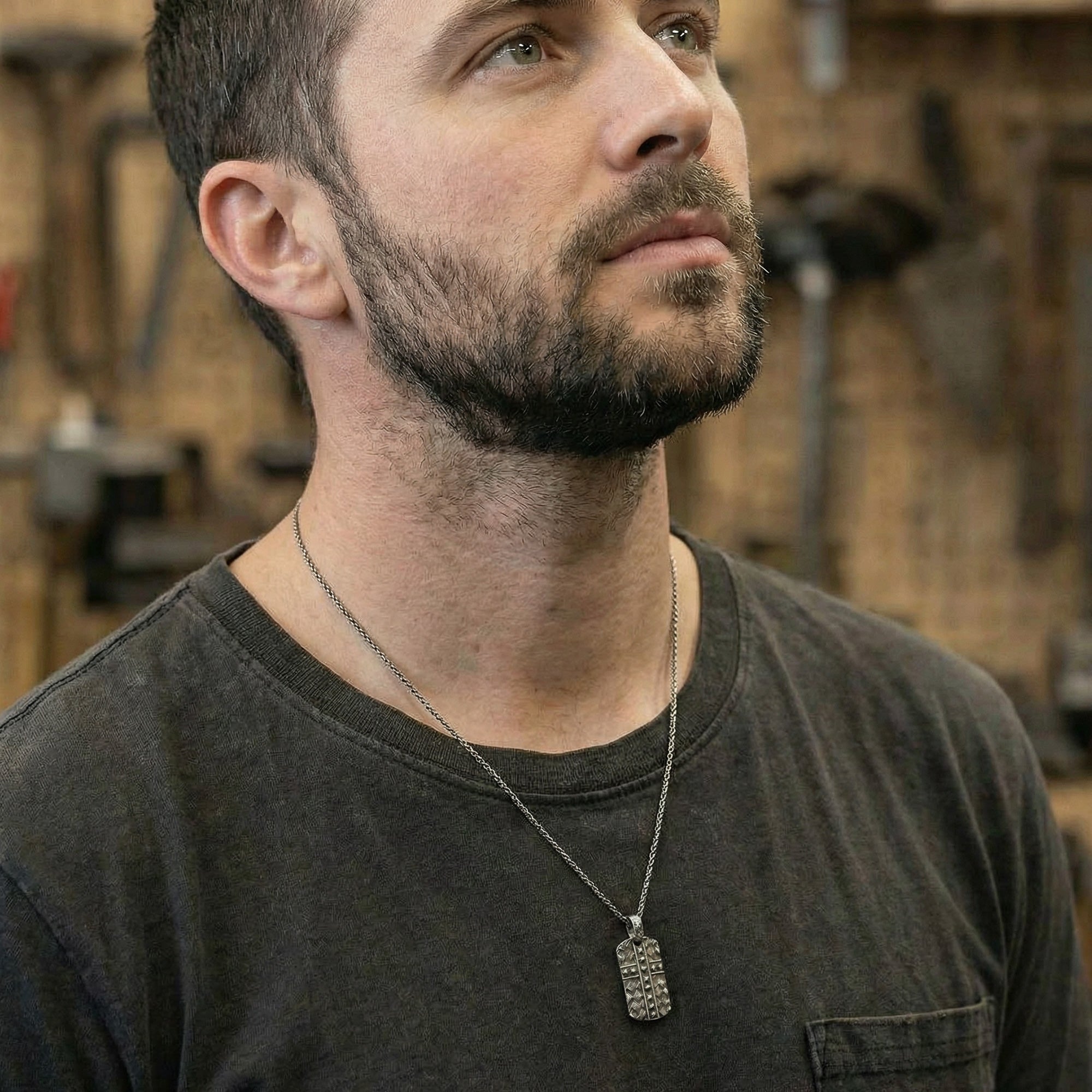 Man in a woodworking workshop wearing black steel men's cross dog tag necklace looking up to the ceiling.