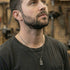 Man in a woodworking workshop wearing black steel men's cross dog tag necklace looking up to the ceiling.