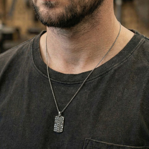 Close-up of a man wearing black steel men's cross dog tag necklace.
