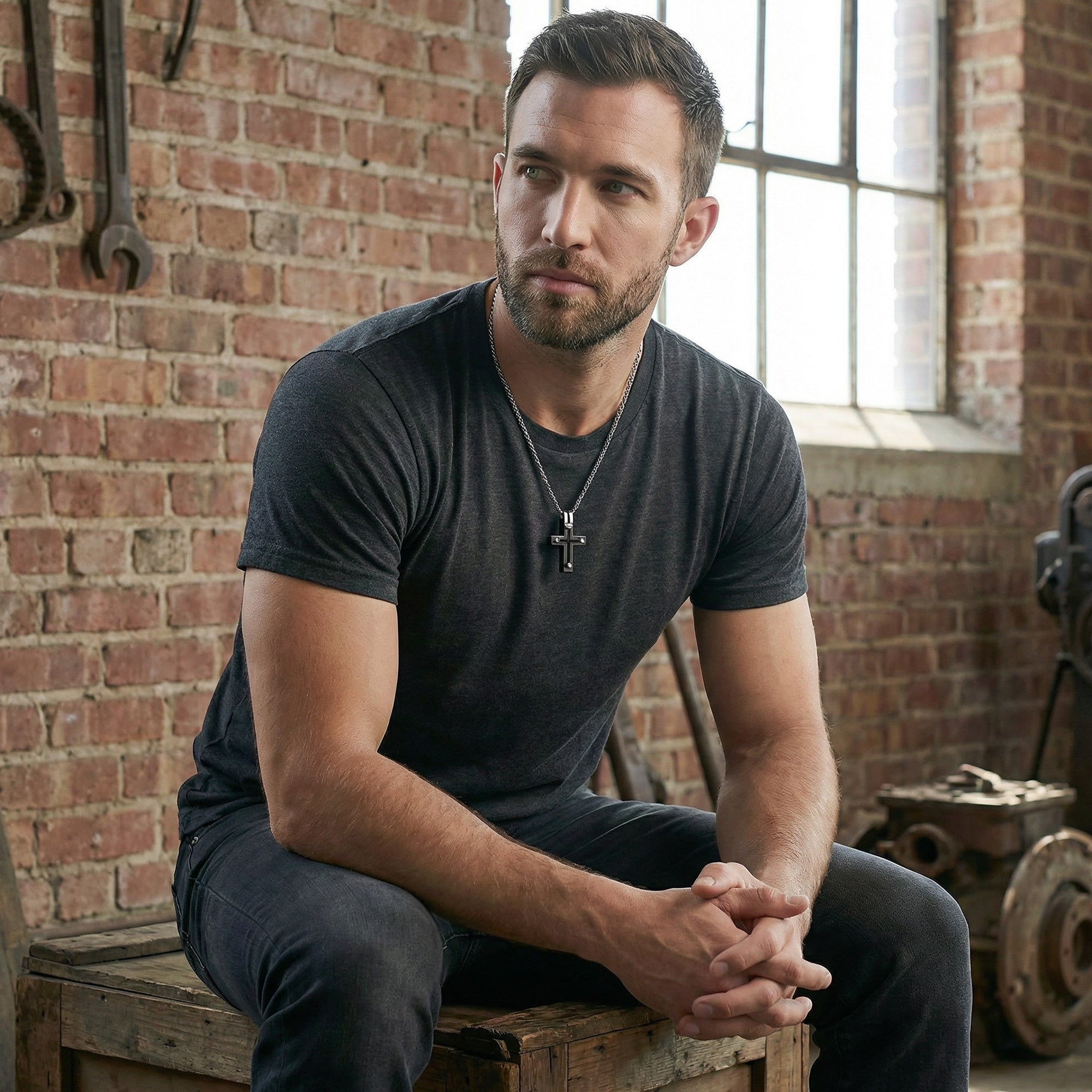 Man sitting on a wooden crate wearing black rivet cross stainless steel necklace.