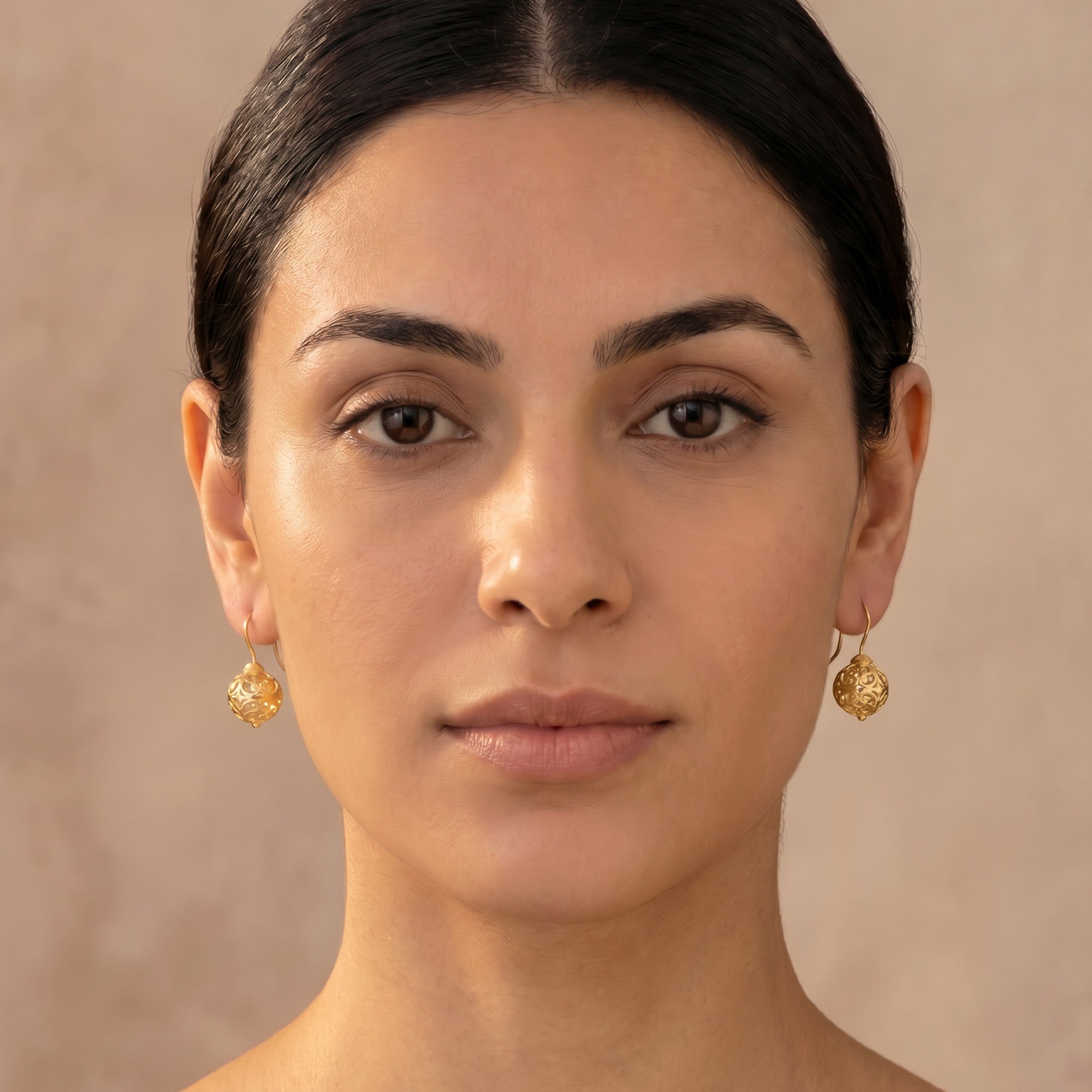Woman wearing a pair of Engelsrufer cage ball gold hook earrings.