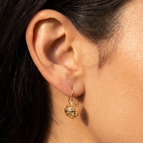 Woman wearing Engelsrufer cage ball gold hook earrings.