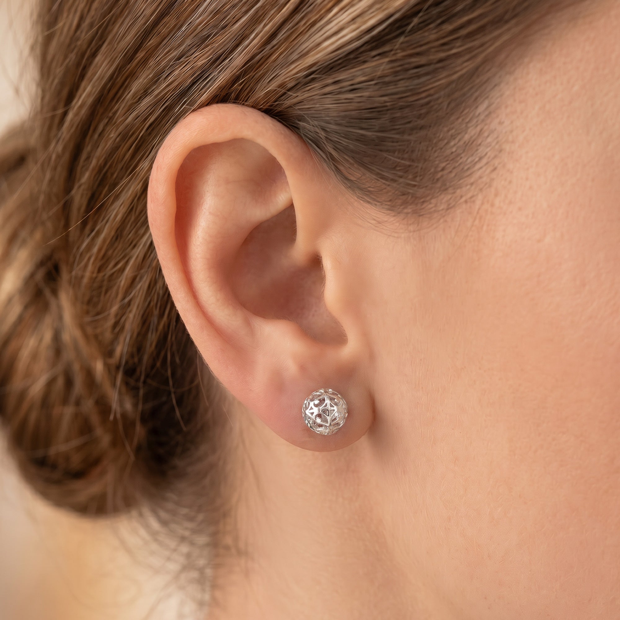 Woman wearing Engelsrufer filigree cage ball silver stud earrings.