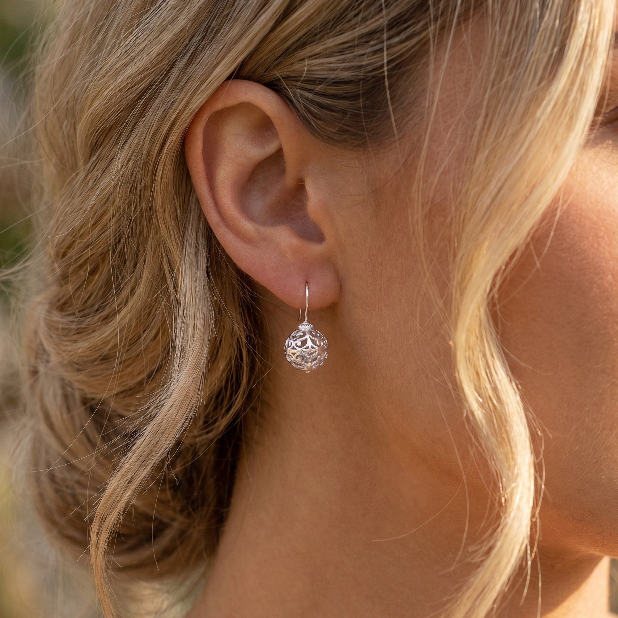 Close-up of a woman wearing Engelsrufer cage ball silver hook earrings.