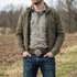 Man standing in a field with his hands in his pockets wearing a belt with a Celtic green man face belt buckle.