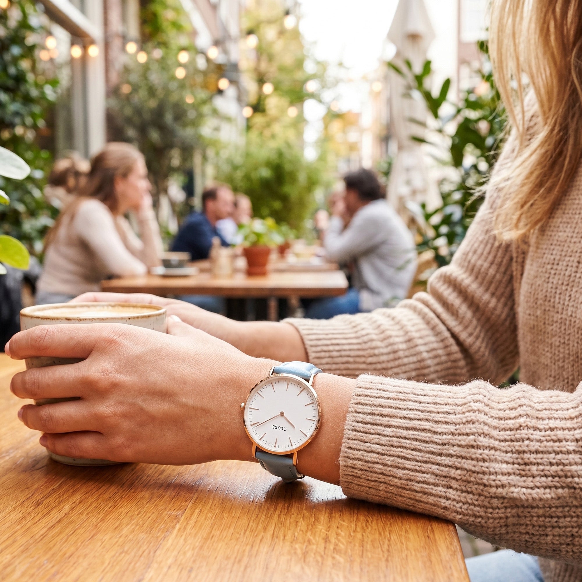 Woman wearing Cluse La Boheme rose gold white/pastel baby blue watch at an outdoor restaurant.