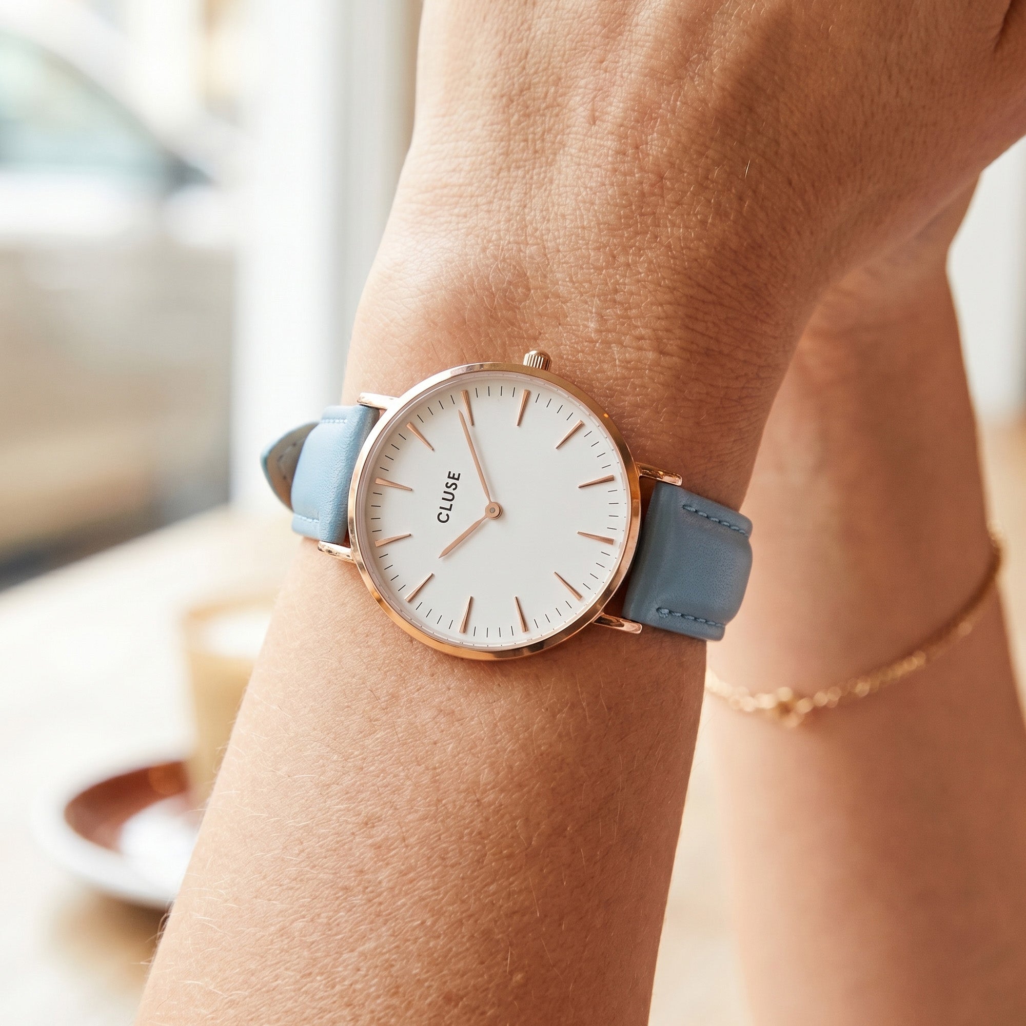 Woman wearing Cluse La Boheme rose gold white/pastel baby blue watch.