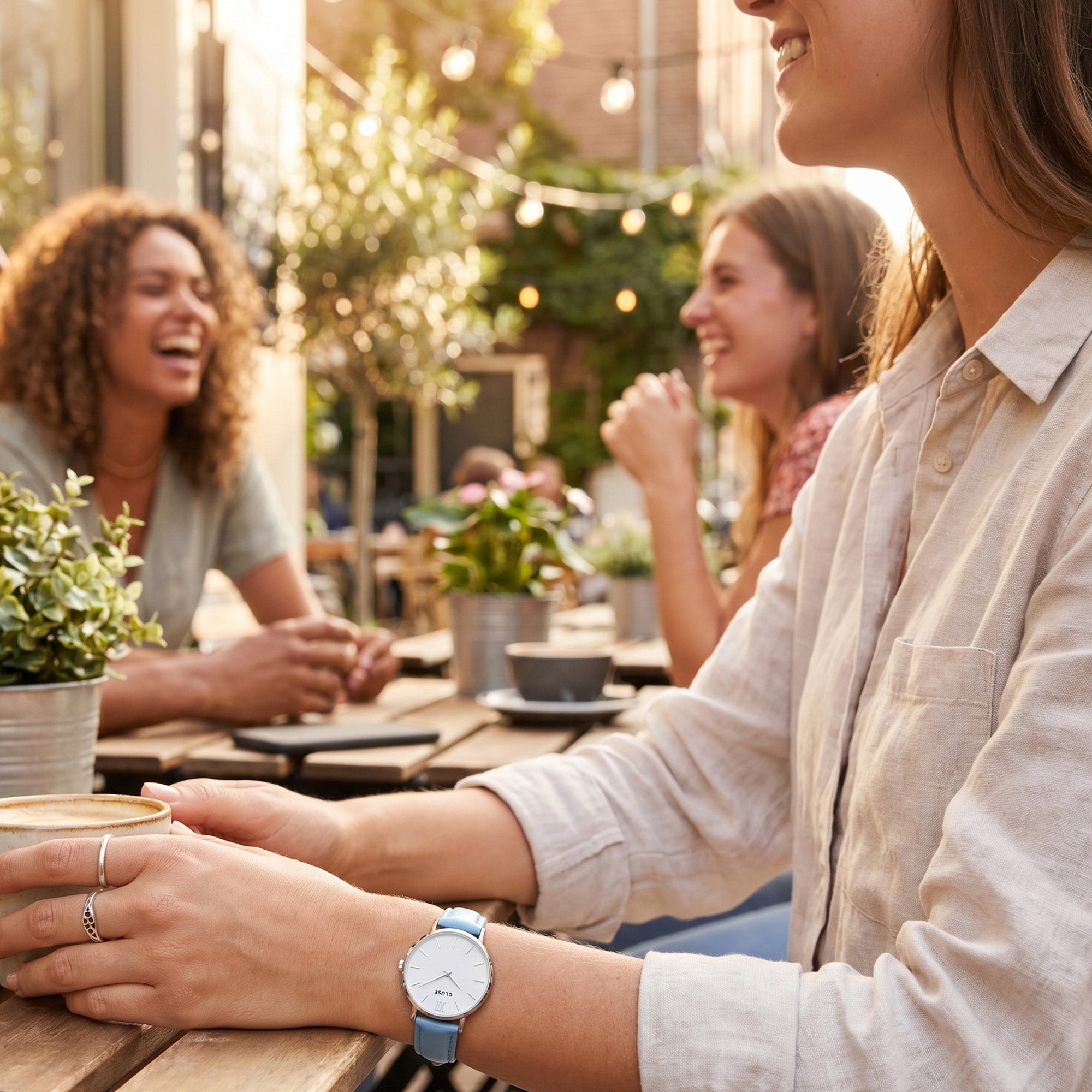 Woman wearing Cluse Minuit silver/white baby blue watch at an outdoor cafe.