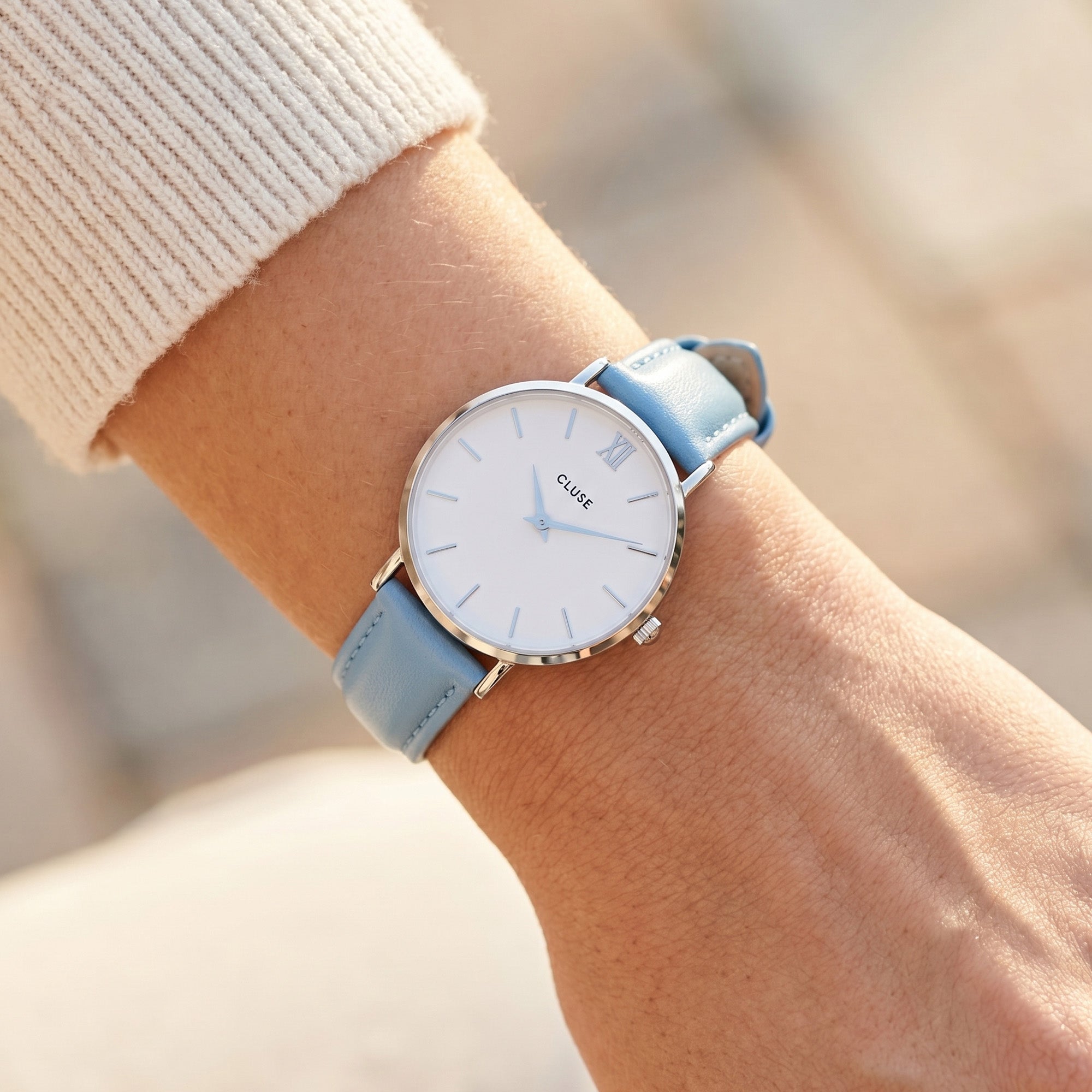 Woman wearing Cluse Minuit silver/white baby blue watch on her wrist.
