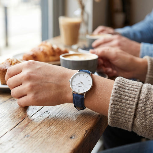Woman wearing Cluse Minuit silver/white denim watch at an indoor cafe.