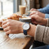 Woman wearing Cluse Minuit silver/white denim watch at an indoor cafe.