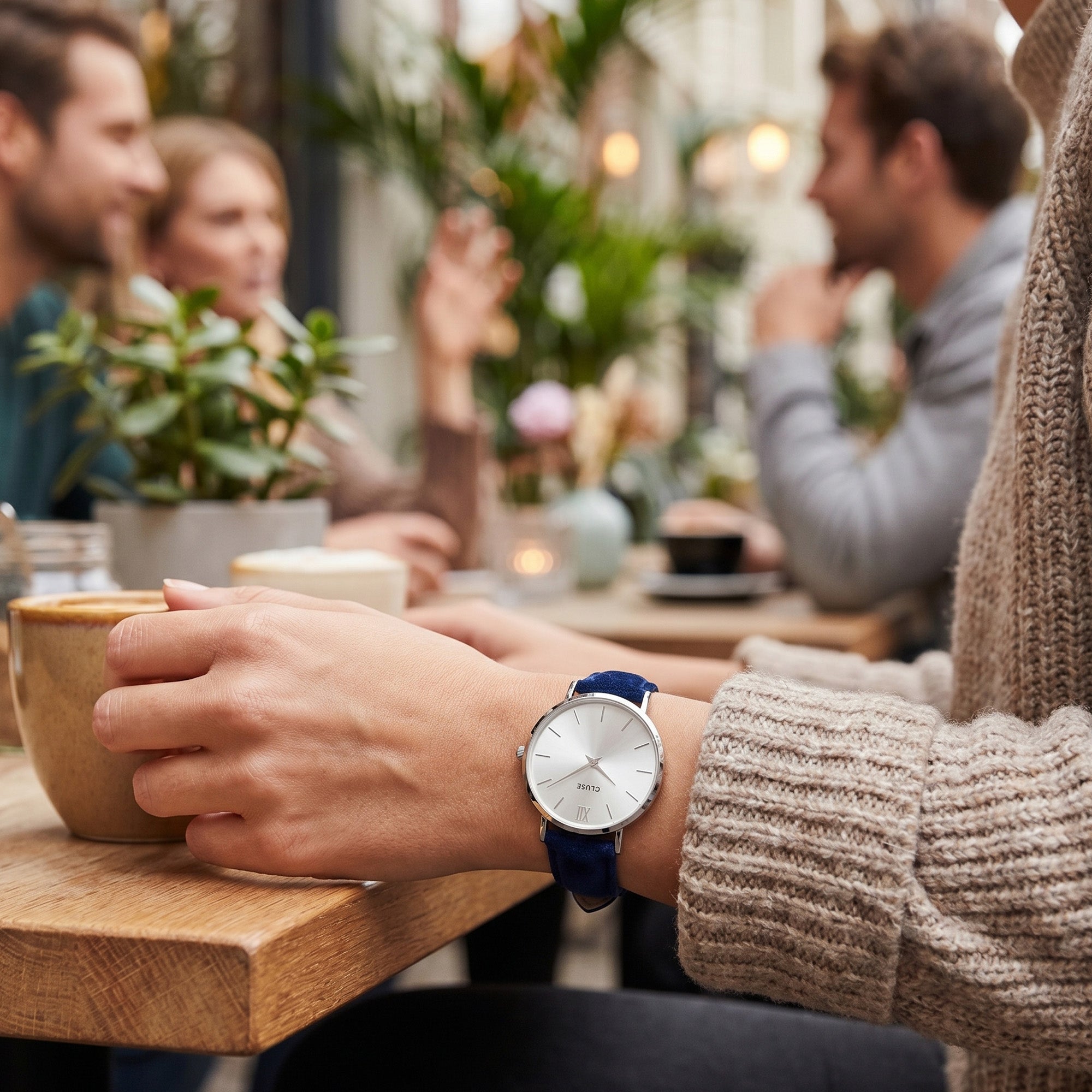 Woman wearing Cluse Minuit silver blue velvet limited edition watch at an outdoor cafe.