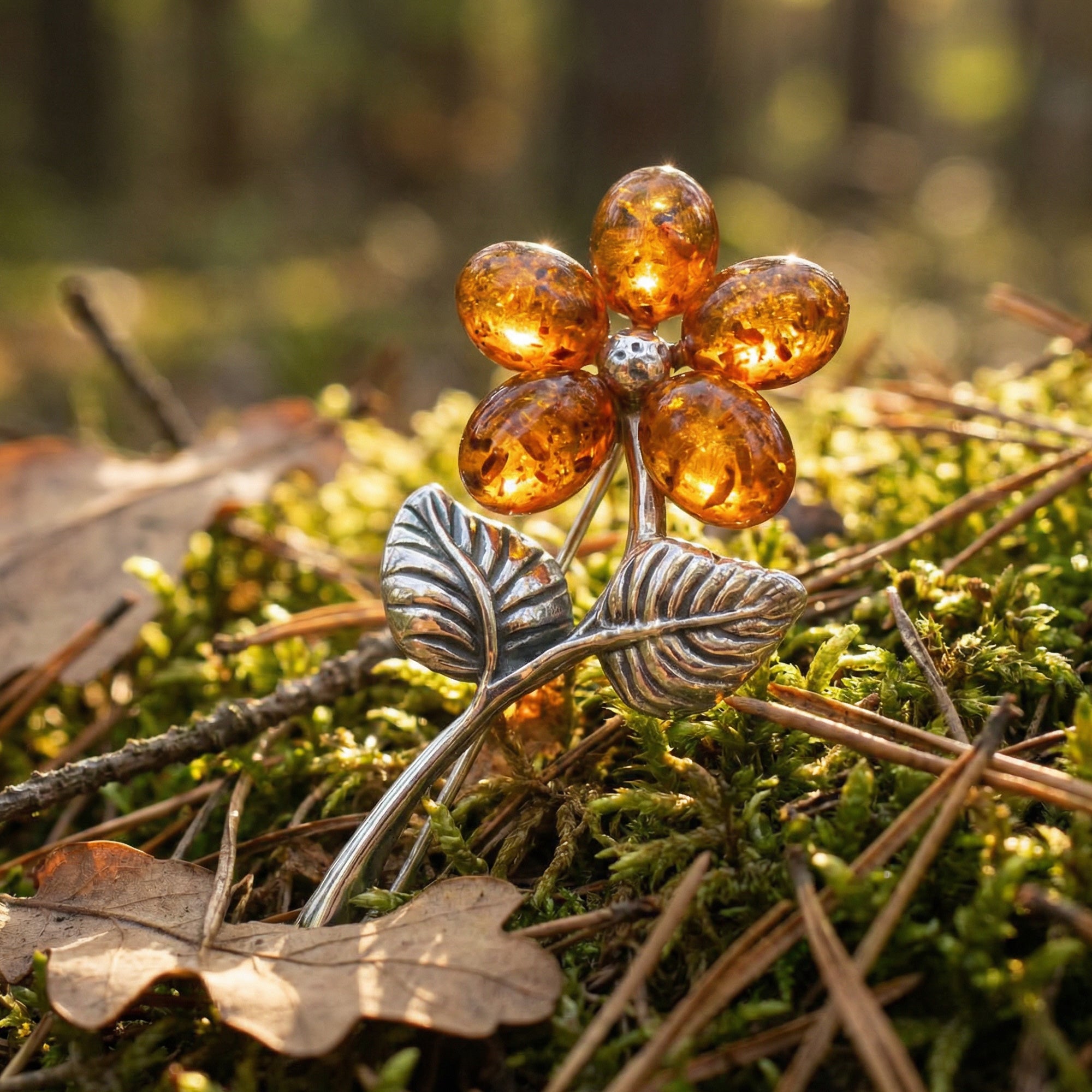 A cognac Baltic amber sterling silver flower brooch basked in sunlight amidst twigs and green moss.