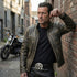 Biker man leaning against a brick wall wearing a black leather belt with a Celtic cross shield, dagger and skull belt buckle.