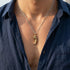 Close up of a man in an open-neck shirt wearing a gold dragon tooth men's necklace.