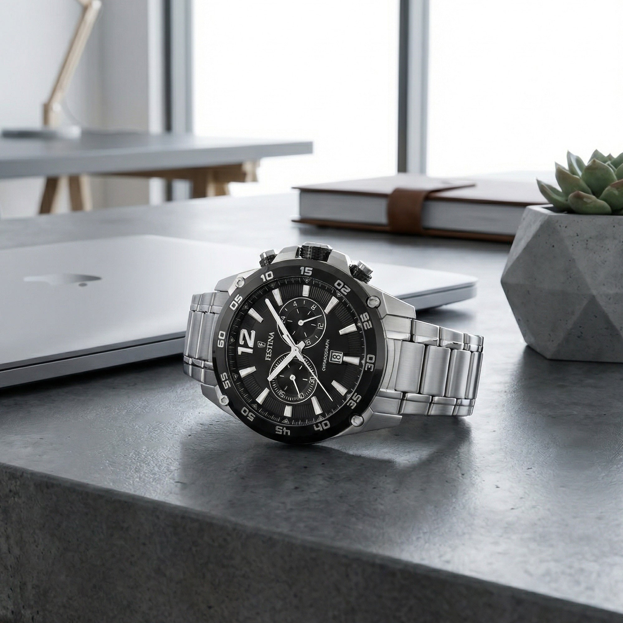 Festina men's black dial chronograph date watch on a concrete desk in a modern office.