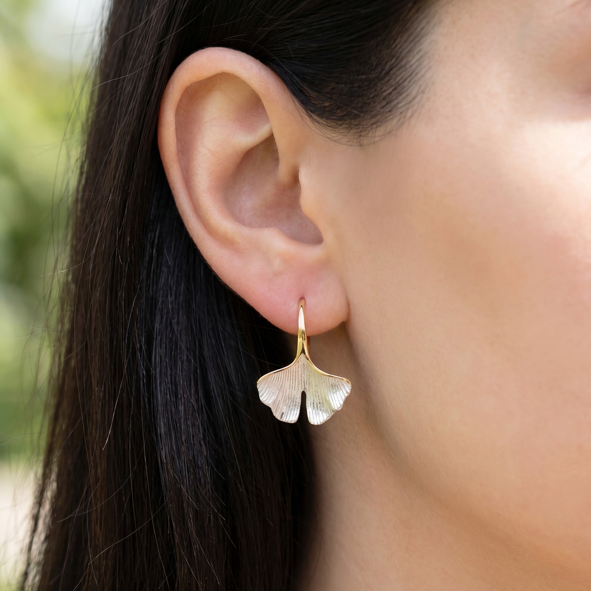 Woman wearing Engelsrufer gold ginkgo leaf hook earrings.