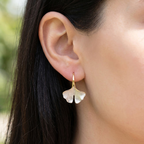 Woman wearing Engelsrufer gold ginkgo leaf hook earrings.