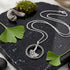 Engelsrufer ginkgo leaf marcasite circle necklace laying on a black marble surface with green ginkgo leaves.
