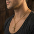 Close-up side profile of man wearing Byzantine rope knot cross gold stainless steel necklace.