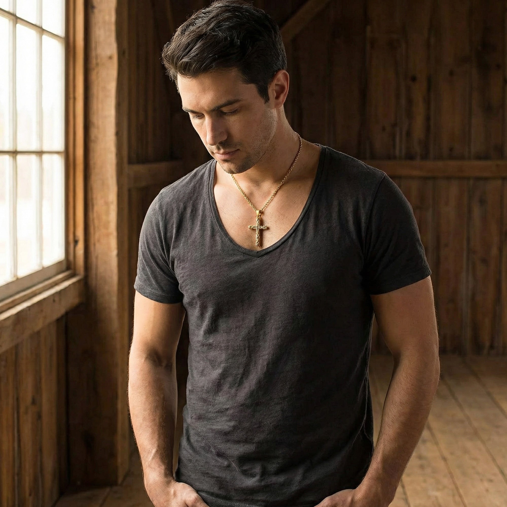 Man standing next to a window looking pensive wearing Byzantine rope knot cross gold stainless steel necklace.
