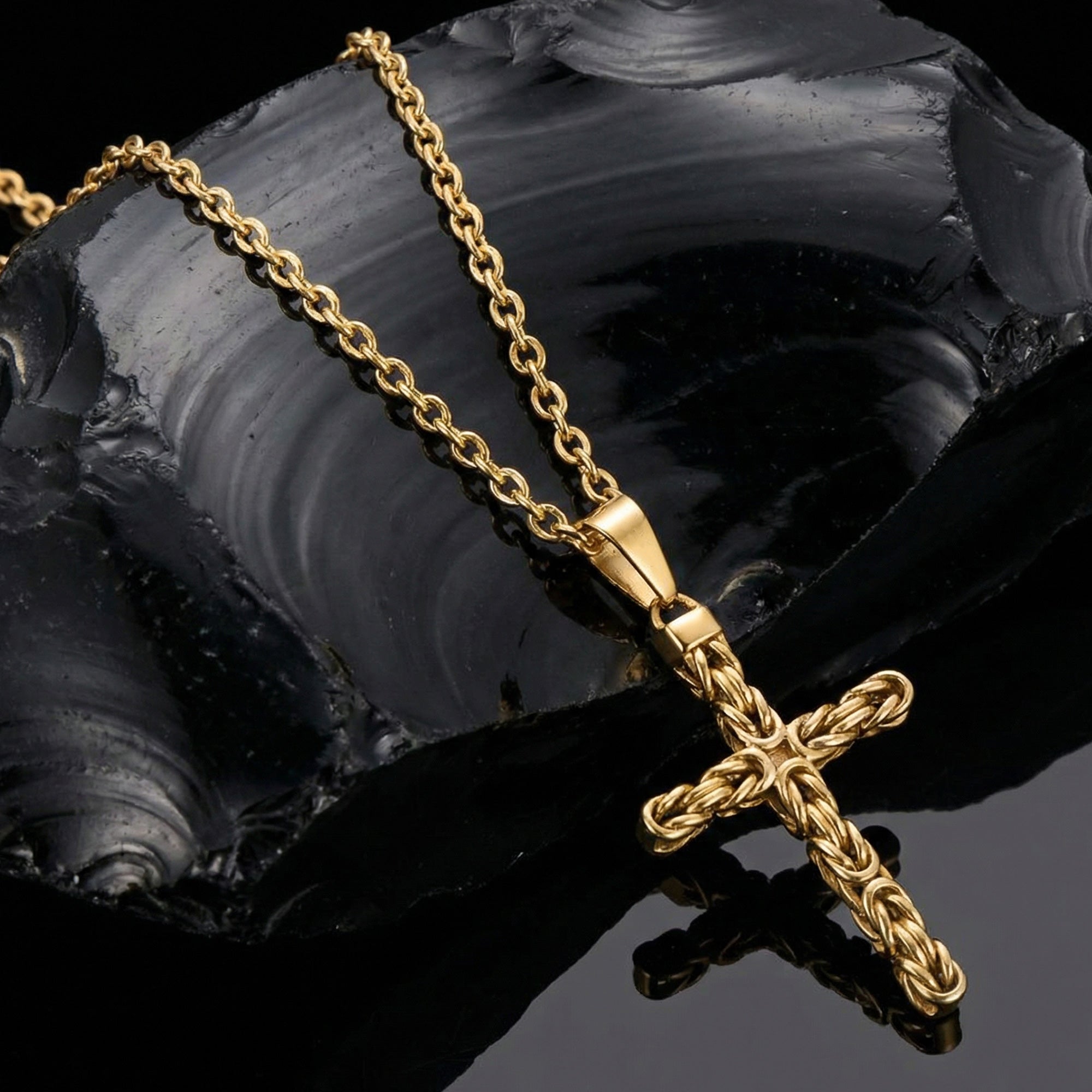 Byzantine rope knot cross men's gold stainless steel necklace laying on black obsidian rock.