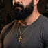 Close-up of a bearded man in a t-shirt wearing barbed cross gold steel necklace.